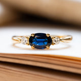 A vintage three-stone sapphire and diamond yellow gold engagement ring, displayed on book pages. 
