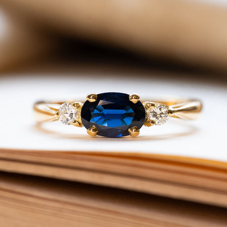A vintage three-stone sapphire and diamond yellow gold engagement ring, displayed on book pages. 