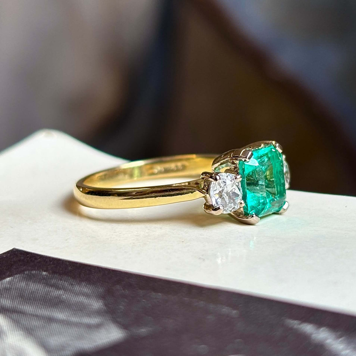 Vintage, emerald and diamond three-stone engagement ring on vintage book with blurred background. 