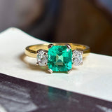Vintage, emerald and diamond three-stone engagement ring on vintage book with blurred background. 