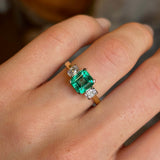 Vintage, emerald and diamond three-stone engagement ring worn on hand close up. 