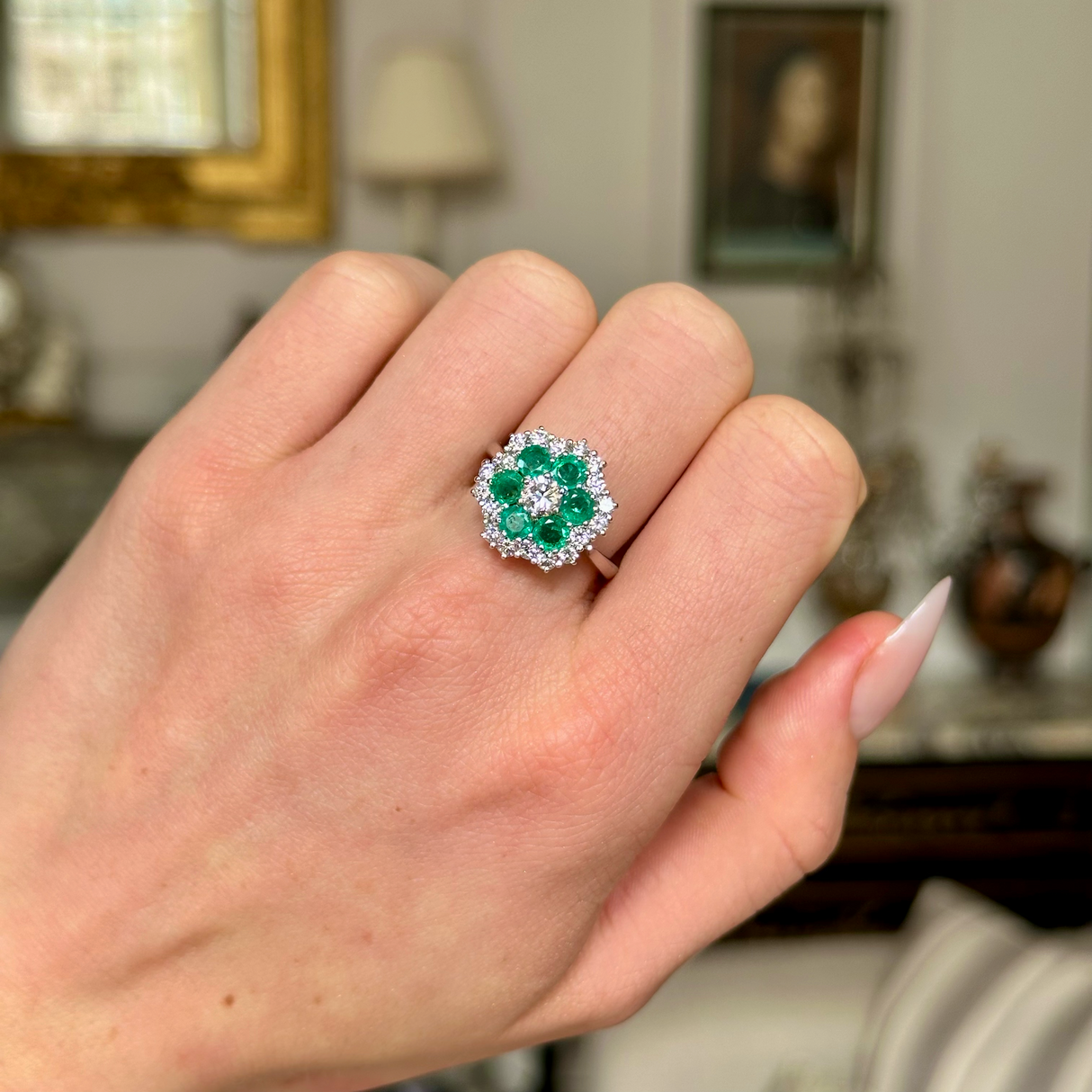 Vintage emerald and diamond cluster ring worn on closed hand, front view. 