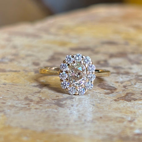 Another front view of a yellow-brown tinted old mine-cut diamond cluster engagement ring, showcasing a vintage-inspired design, displayed on a textured background to showoff the brown tones in the central diamond, all set in yellow gold.