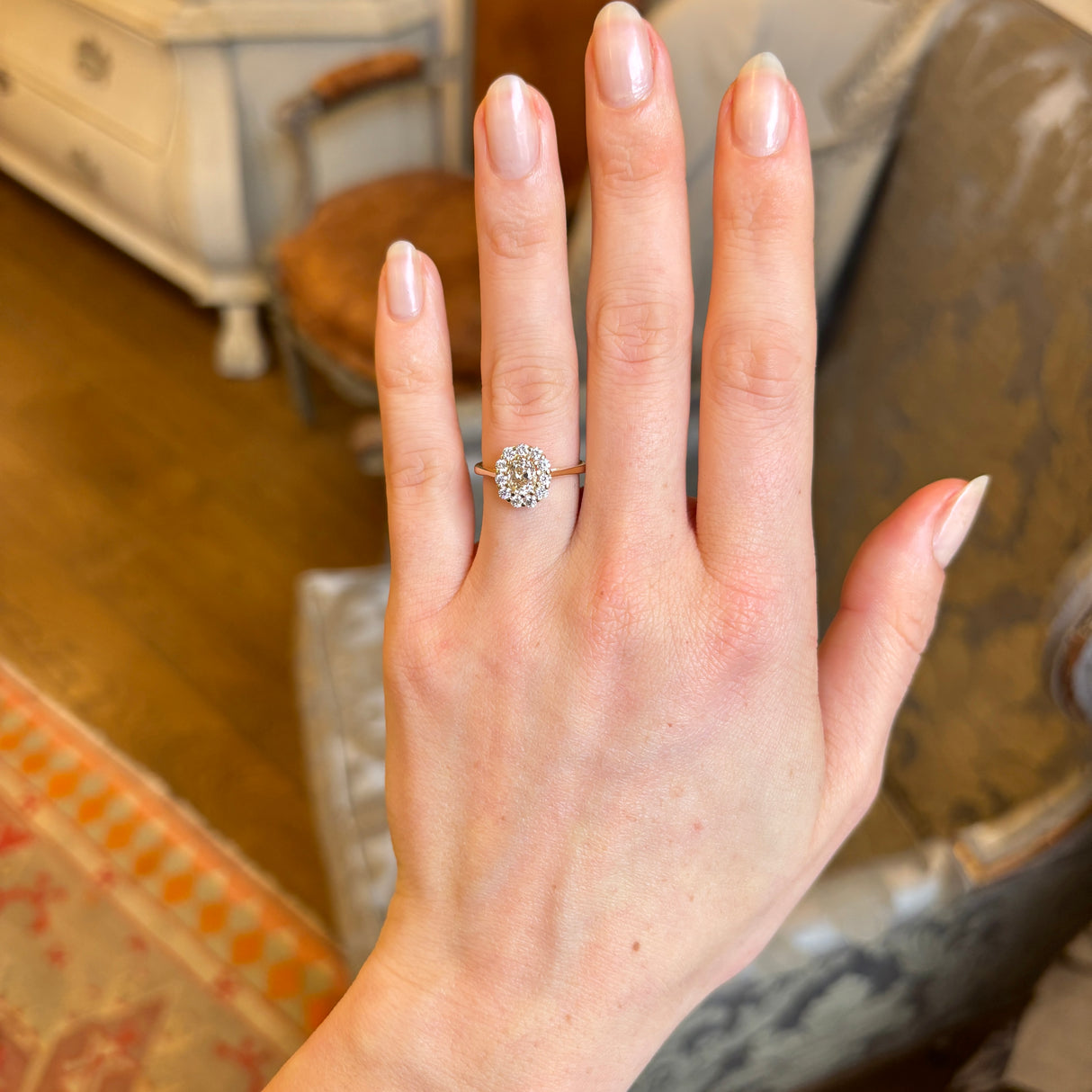 A woman’s hand displaying the yellow-brown tinted old mine-cut diamond cluster engagement ring on the engagement ring finger, viewed from a distance in natural light