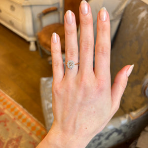 A woman’s hand displaying the yellow-brown tinted old mine-cut diamond cluster engagement ring on the engagement ring finger, viewed from a distance in natural light