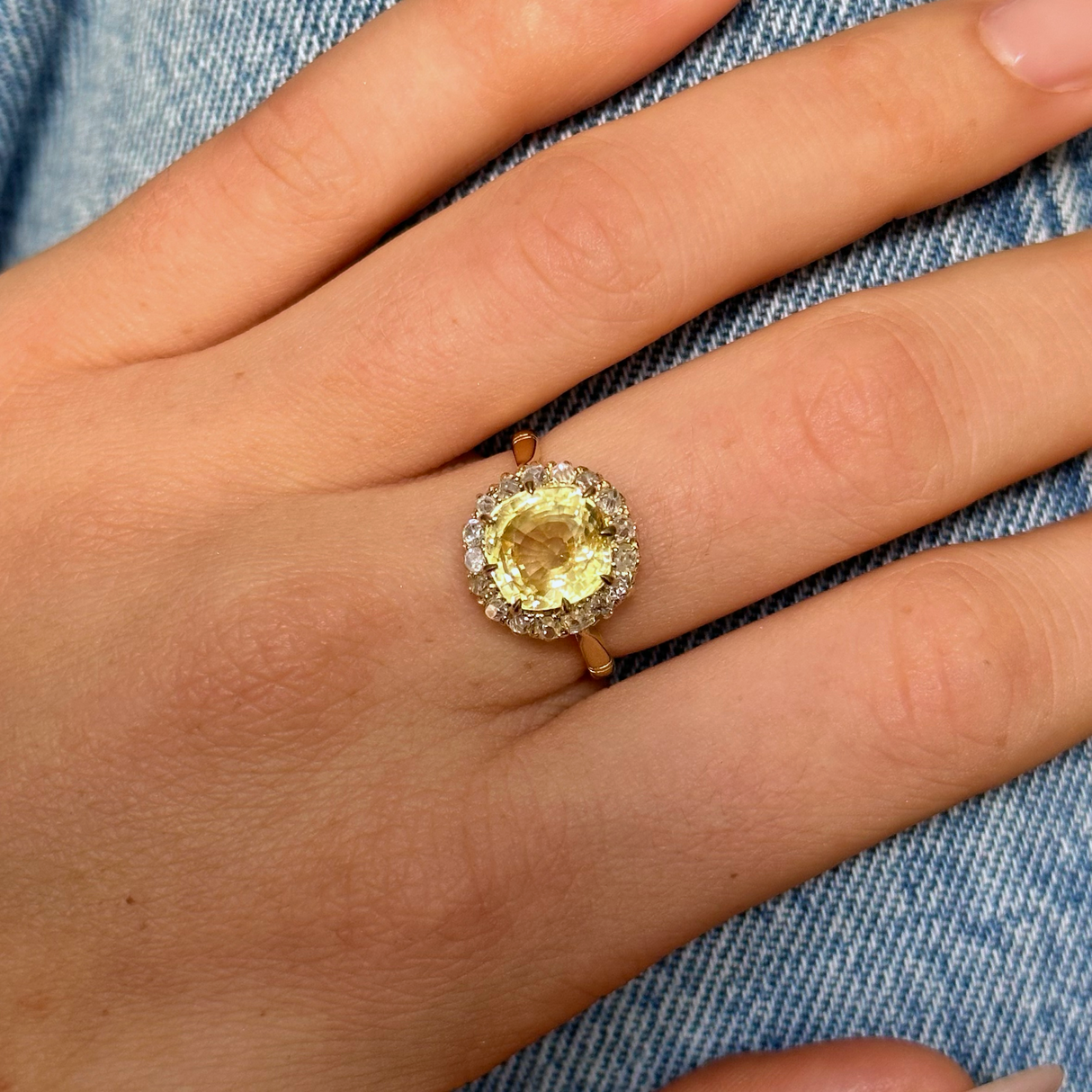 Vintage, Cushion-cut Yellow Sapphire Diamond Cluster Engagement Ring, worn on hand placed on denim jeans, front view. 