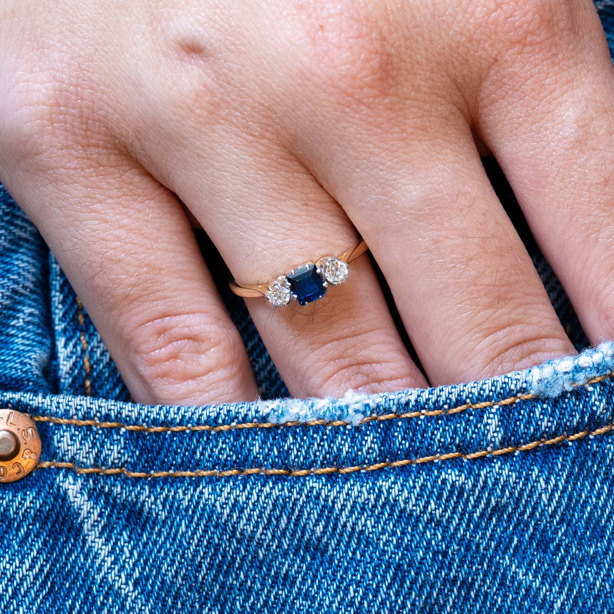 Antique 1920s sapphire and diamond three-stone ring worn with hand resting in denim pocket.