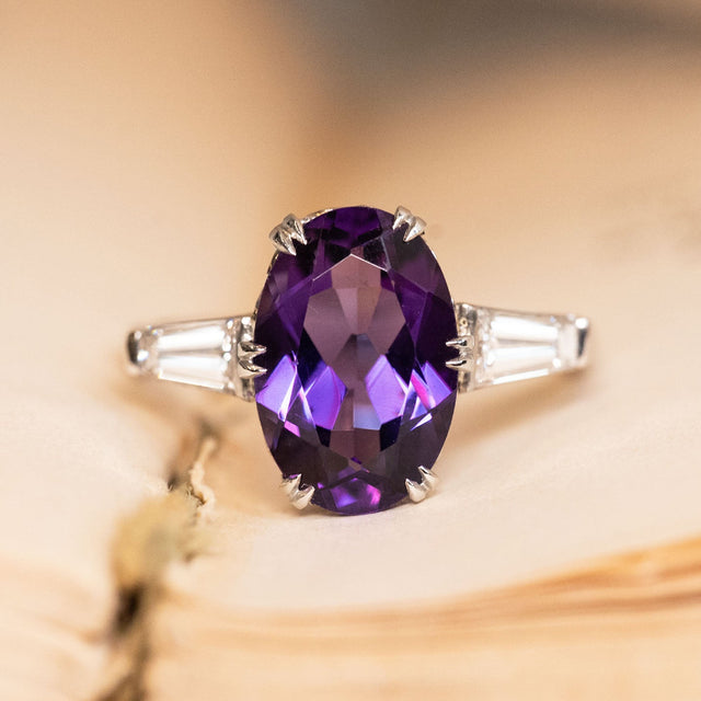Antique Art Deco amethyst and diamond three-stone ring featuring an oval-cut amethyst flanked by tapered baguette diamonds in platinum.