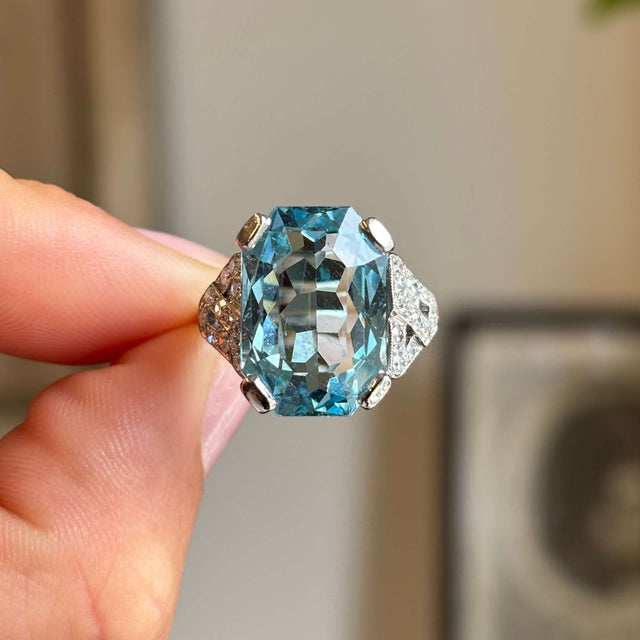 Close-up of an antique Art Deco aquamarine and diamond cocktail ring in platinum, featuring a striking aquamarine centre stone flanked by brilliant-cut diamonds against a softly lit background.