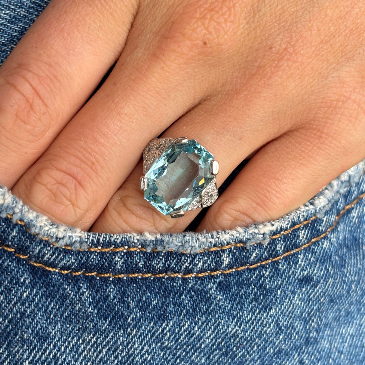 Antique Art Deco aquamarine and diamond cocktail ring in platinum photographed on hand against blue denim, showcasing the vivid aquamarine centre and elegant diamond cluster design.