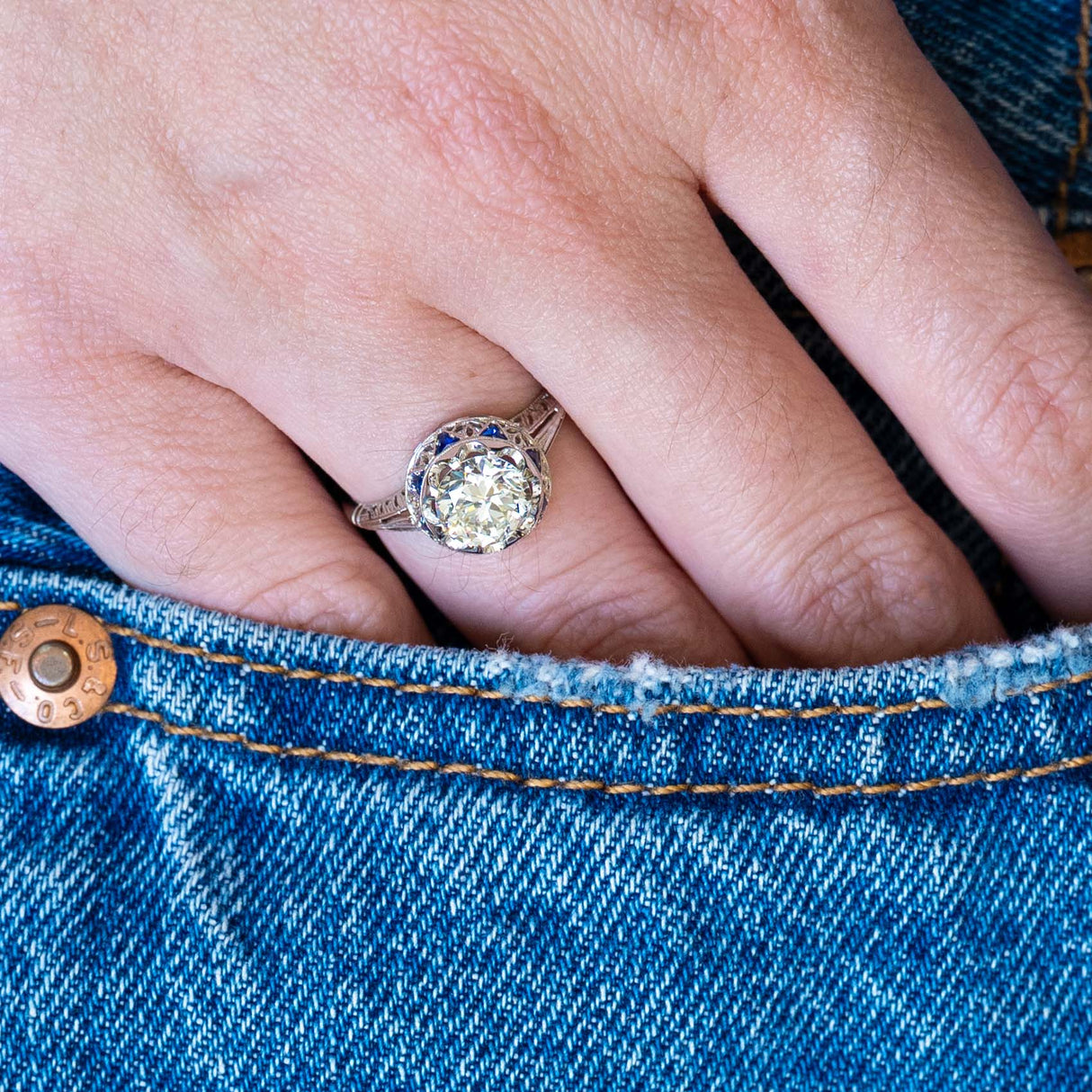 Antique Art Deco diamond and sapphire cluster ring worn on hand with blue denim pocket detail.