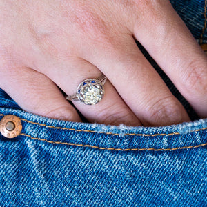 Antique Art Deco diamond and sapphire cluster ring worn on hand with blue denim pocket detail.