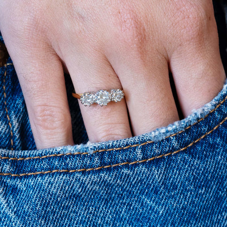 Antique Art Deco diamond three-stone ring worn with hand resting in denim pocket.
