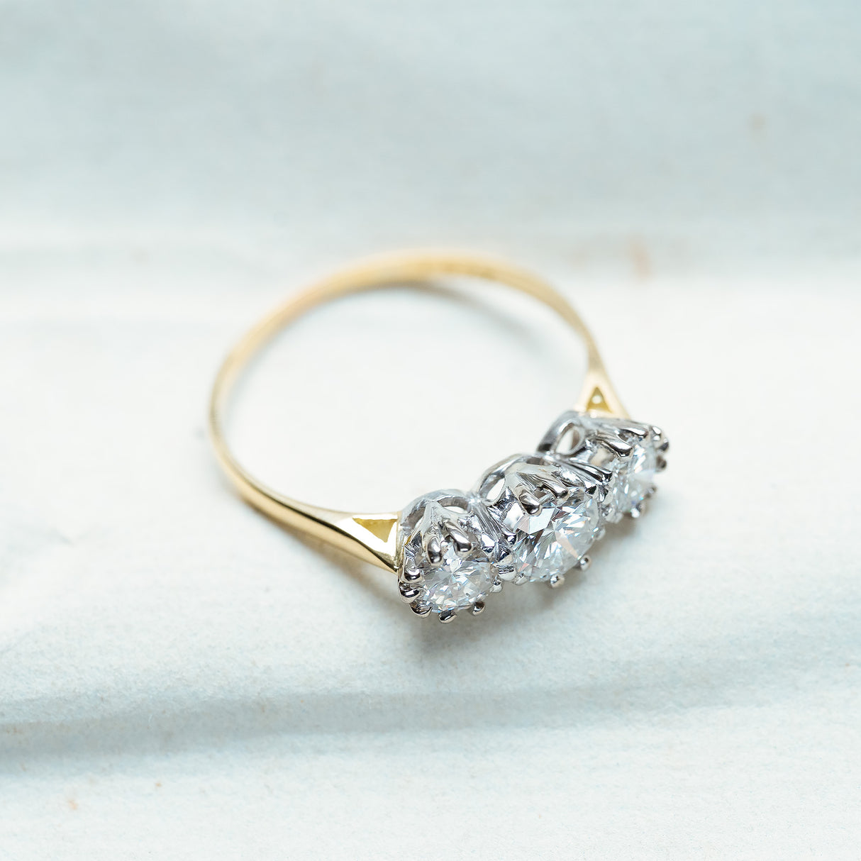 Antique Art Deco diamond three-stone ring with raised diamond setting and fine gold band.