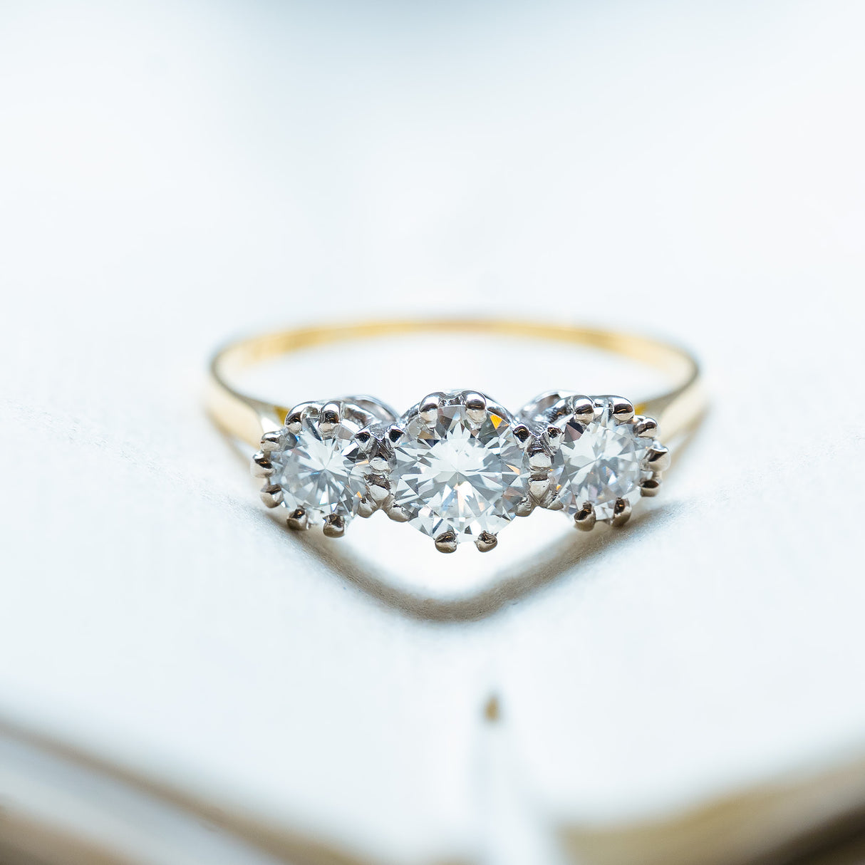 Antique Art Deco diamond three-stone ring resting on open book pages.