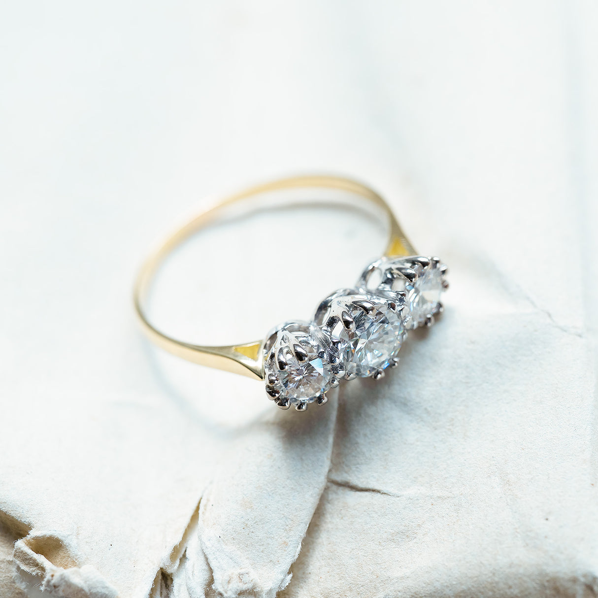 Antique Art Deco diamond three-stone ring styled on textured paper background.