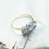 Antique Art Deco diamond three-stone ring styled on textured paper background.