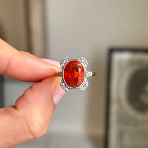 Antique Art Deco fire opal and diamond cluster ring featuring a vibrant fire opal surrounded by a halo of diamonds, held by hand.