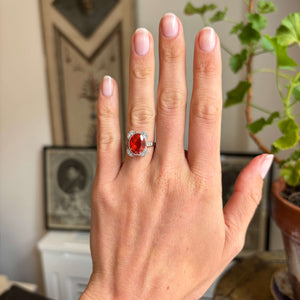 Antique Art Deco fire opal and diamond cluster ring with a vivid fire opal centre stone and diamond halo, displayed on a hand.