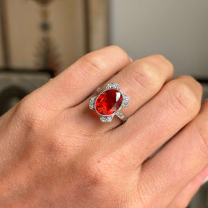 Antique Art Deco fire opal and diamond cluster ring featuring a fiery orange-red opal encircled by diamonds, worn on a hand.