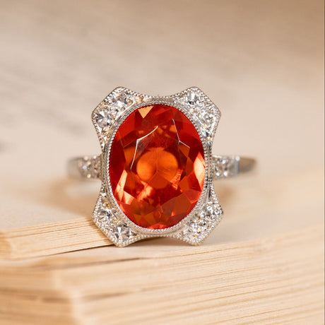Antique Art Deco fire opal and diamond cluster ring featuring a vivid orange fire opal framed by old-cut diamonds in a geometric platinum setting.