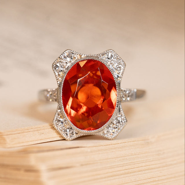 Antique Art Deco fire opal and diamond cluster ring featuring a vivid orange fire opal framed by old-cut diamonds in a geometric platinum setting.