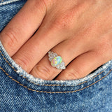 Antique Art Deco opal and diamond cluster ring photographed on hand against denim, highlighting the iridescent opal and brilliant diamond surround.