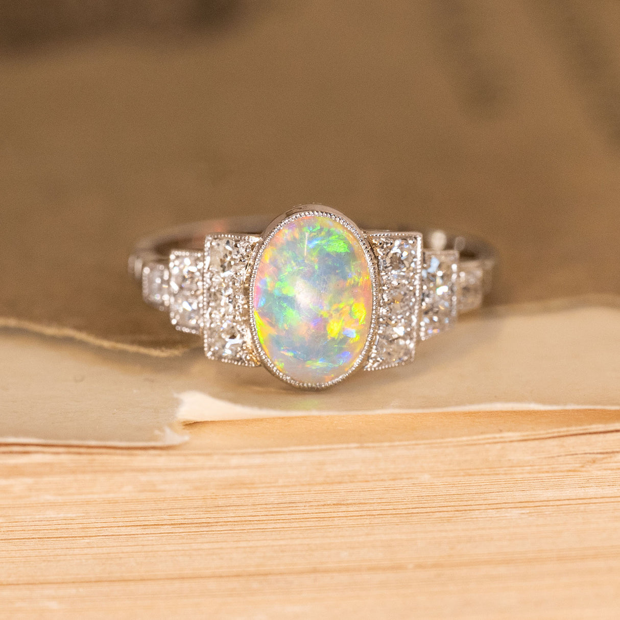 Antique Art Deco opal and diamond cluster ring featuring an oval opal displaying vivid flashes of green, blue and orange, framed by old-cut diamonds in a geometric setting.