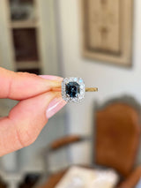 Antique Art Deco sapphire and diamond cluster engagement ring featuring a blue sapphire centre stone surrounded by a geometric diamond cluster, held by hand.
