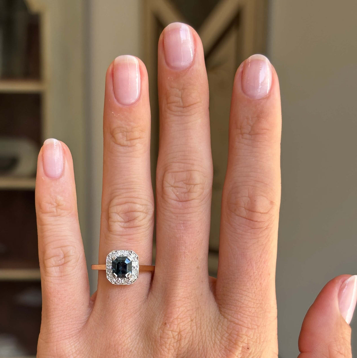 Antique Art Deco sapphire and diamond cluster engagement ring with a blue sapphire centre and diamond cluster surround, displayed on a hand.