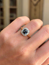 Antique Art Deco sapphire and diamond cluster engagement ring featuring a blue sapphire centre stone and geometric diamond cluster design, worn on a hand.