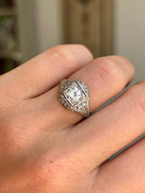 Platinum Art Deco diamond cluster ring with antique diamond detailing on a hand with blurred background