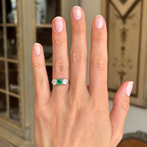 Antique Edwardian emerald and diamond three-stone engagement ring with an emerald centre stone and diamond side stones, displayed on a hand.
