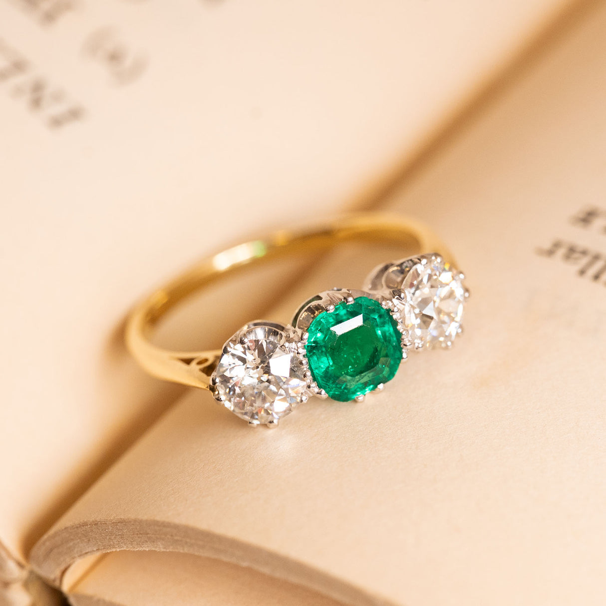 Edwardian emerald and diamond ring showcasing a vibrant round emerald between a pair of sparkling old-cut diamonds.