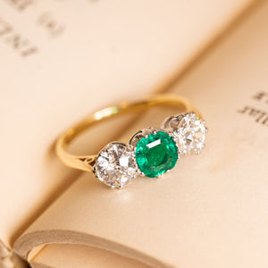 Edwardian emerald and diamond ring showcasing a vibrant round emerald between a pair of sparkling old-cut diamonds.