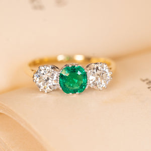 Antique Edwardian three-stone ring featuring a vivid green emerald flanked by two old-cut diamonds in a refined yellow gold setting.