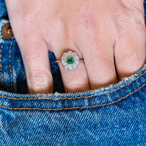 Antique Edwardian emerald and old-mine cut diamond cluster ring worn with hand resting in denim pocket.