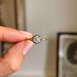 Antique Edwardian old-cut diamond daisy cluster ring held between fingers, featuring a sparkling old-cut diamond centre surrounded by a daisy-shaped diamond halo.