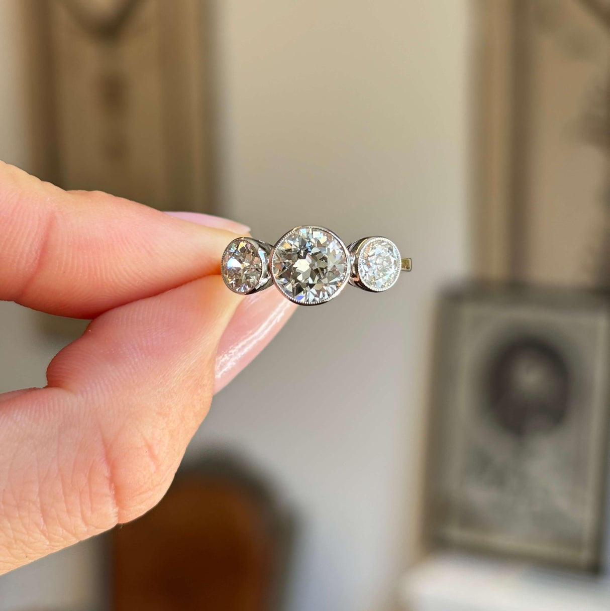 Antique Edwardian old-cut diamond three-stone engagement ring featuring three old-cut diamonds in a classic trilogy setting, held by hand.