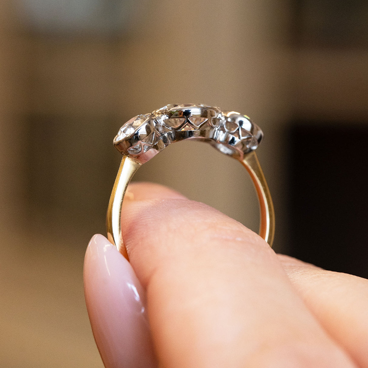 Antique Edwardian old cut diamong gold ring held by a hand against a blurred background.