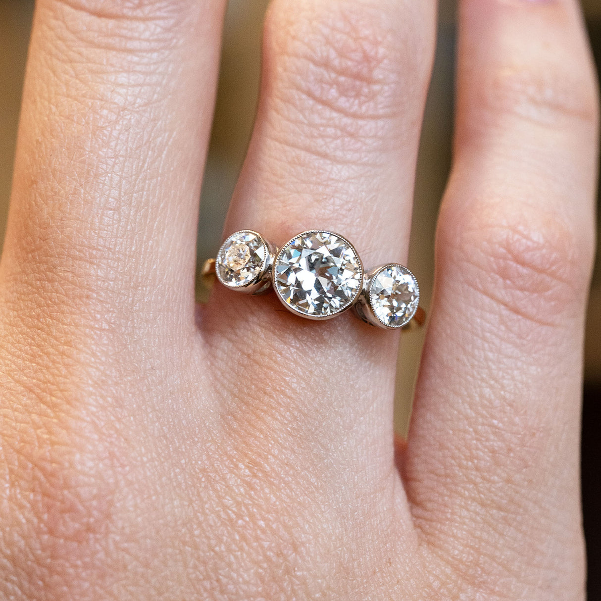 Antique, Edwardian old-cut diamond three-stone engagement ring showcased on a ring finger on a hand.