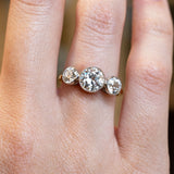 Antique, Edwardian old-cut diamond three-stone engagement ring showcased on a ring finger on a hand.