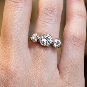 Antique, Edwardian old-cut diamond three-stone engagement ring showcased on a ring finger on a hand.