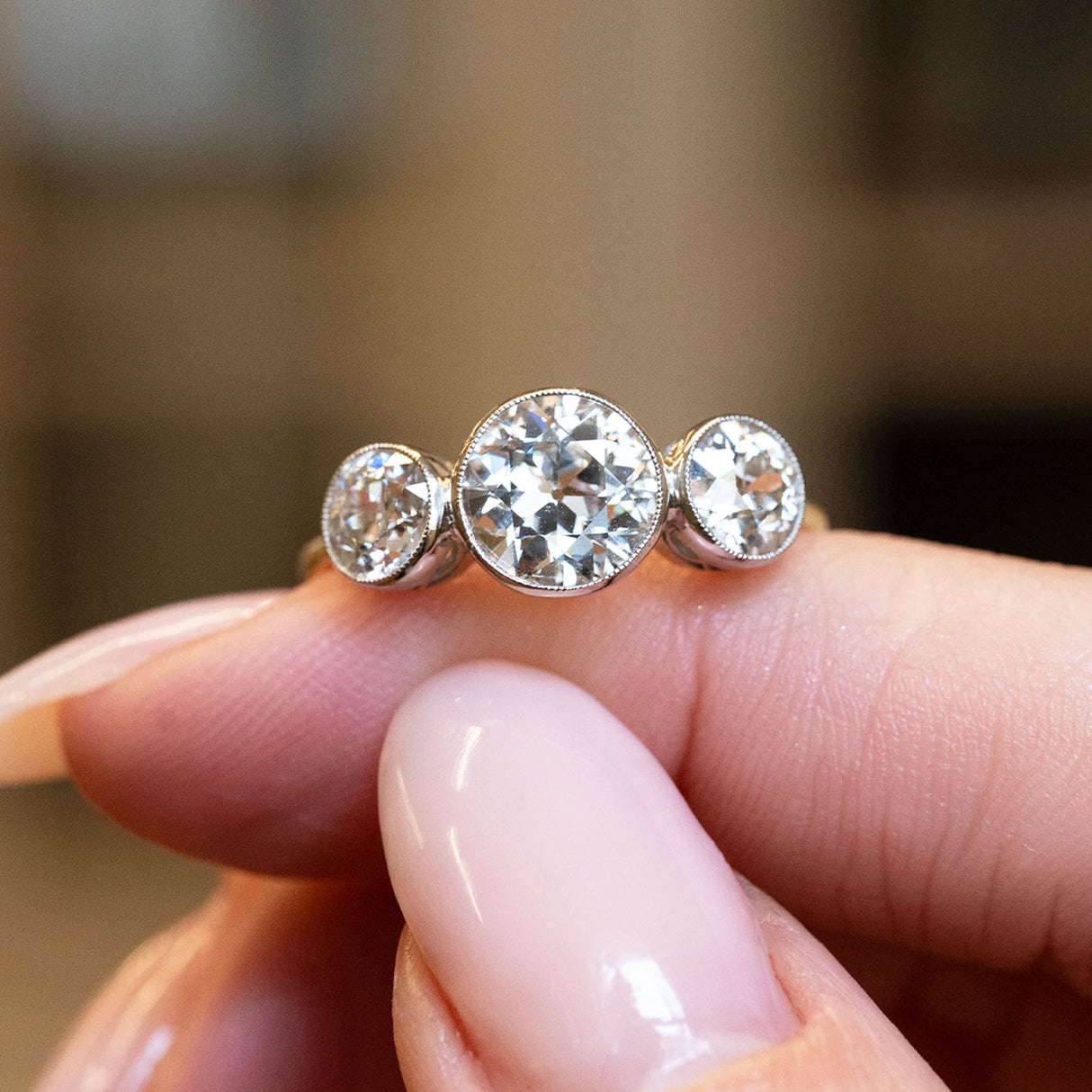 Antique, Edwardian old-cut diamond three-stone engagement ring shown on a finger.