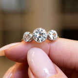 Antique, Edwardian old-cut diamond three-stone engagement ring shown on a finger.