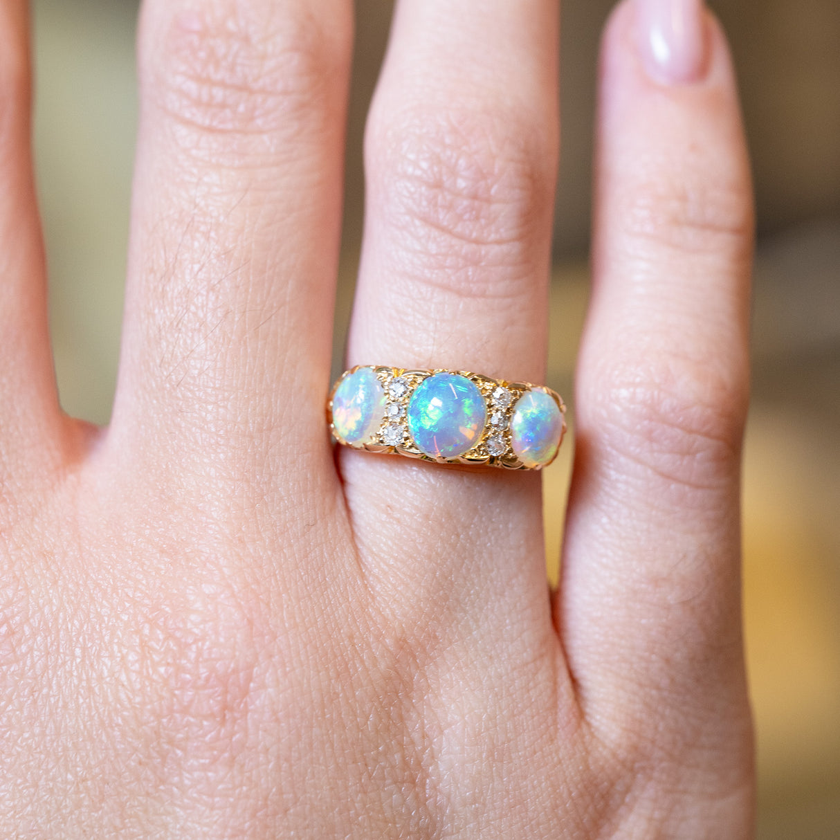 Antique Edwardian opal and diamond three-stone ring with glowing opals and gold band.