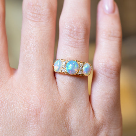 Antique Edwardian opal and diamond three-stone ring with glowing opals and gold band.