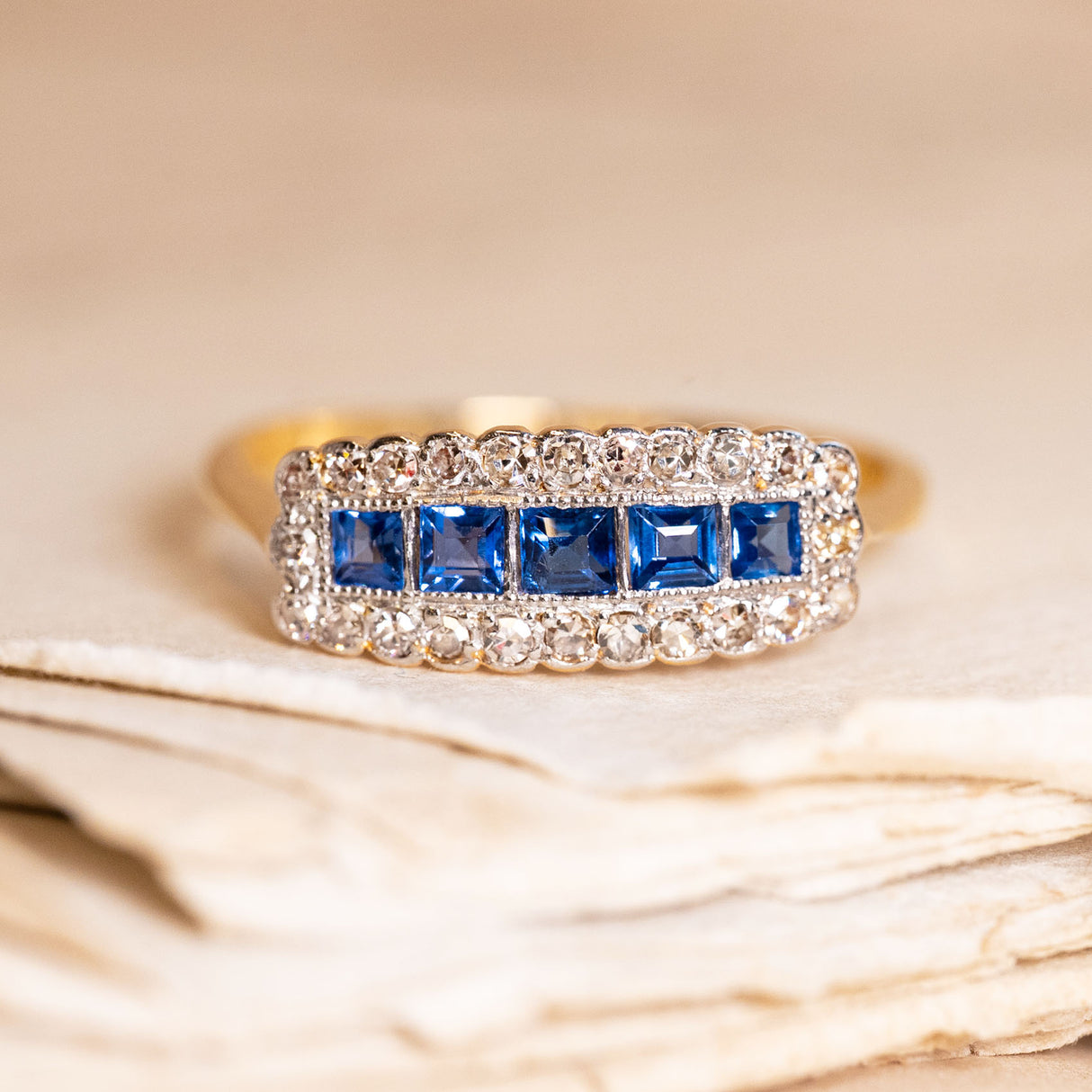 Antique Edwardian sapphire and diamond cluster ring featuring calibré-cut blue sapphires framed by old-cut diamonds in a rectangular cluster design.