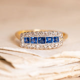 Antique Edwardian sapphire and diamond cluster ring featuring calibré-cut blue sapphires framed by old-cut diamonds in a rectangular cluster design.