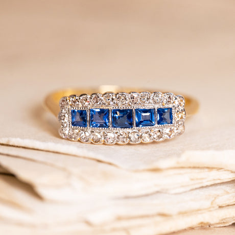 Antique Edwardian sapphire and diamond cluster ring featuring calibré-cut blue sapphires framed by old-cut diamonds in a rectangular cluster design.
